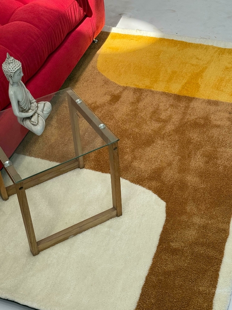 Alfombra Zenith de colores marrón, beige y amarillo, en un ambiente moderno con un sofá rojo y una mesa de vidrio.