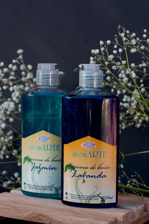 Botellas de espumas de baño aromARTE aromáticas de jazmín y lavanda sobre una superficie de madera, decoradas con flores blancas.
