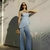 Mulher vestindo conjunto assimétrico azul composto por blusa regata e calça, em ambiente externo iluminado pelo sol.