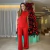Mulher vestindo conjunto feminino de tricô vermelho, composto por regata e calça, em frente a uma árvore de Natal decorada.