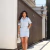 Mulher vestindo conjunto feminino de camisa listrada azul e branca com shorts saia, segurando bolsa branca em ambiente externo.