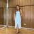 Mulher vestindo conjunto feminino composto por saia lápis midi e cropped azul claro, com botões frontais, em ambiente interno com parede de madeira.
