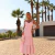 Mulher usando Vestido Midi Laço Garden Rosa em ambiente externo com palmeiras ao fundo, ideal para looks de verão elegantes.