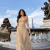 Mulher vestindo conjunto listrado com cropped e saia longa bege e branco, em ponte de Paris com a Torre Eiffel ao fundo.
