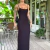 Mulher vestindo um vestido midi preto regata, com alças finas, em ambiente externo com plantas e decoração rústica ao fundo.