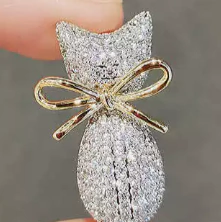 Broche en forma de gato con piedritas brillosas y moño dorado, diseño elegante y brillante para un toque sofisticado.