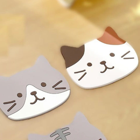 Set de 2 portavasos con caras de gatitos, con diseño kawaii y base antideslizante, ideales para evitar anillos de agua en tu mesa. Calicó con una taza.