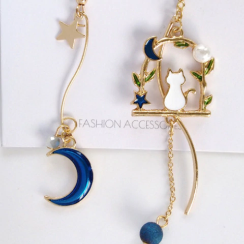 Aretes con gatito blanco en un balcón, media luna azul y estrellita. Acercamiento.