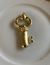 Pingente de chave em dourado, 8cm de comprimento.