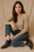 Modelo sentada sobre una superficie suave, vistiendo un suéter beige y jeans, mostrando las botas Charritos Milán de cuero negro con detalles metálicos.