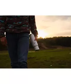 Persona caminando por un paisaje al atardecer, sosteniendo un termo Stanley Adventure To-Go de 1 litro.