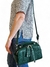 Bolsa feminina tiracolo verde pequena, com alça transversal, sendo carregada por uma mulher vestindo uma blusa com estampa de corações