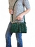 Mulher segurando uma bolsa feminina tiracolo pequena verde, com alça transversal, em frente a um fundo branco.