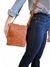 Mulher usando uma bolsa tiracolo caramelo com textura croco, em pé, com blusa listrada e jeans escuro.
