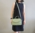 Mulher usando uma bolsa feminina transversal baú média verde menta em couro legítimo, vestida com um vestido preto.