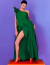 Modelo usando um vestido de festa longo verde com laço, posando em um fundo roxo e degraus laranja.
