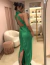 Mulher usando vestido longo verde bandeira com decote americano, vista de costas em um ambiente elegante.
