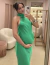 Mulher usando vestido de festa longo verde bandeira com decote americano, tirando selfie em um espelho.