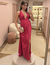 Mulher usando vestido de festa longo de cetim magenta com decote profundo e fenda lateral, segurando uma clutch prateada.