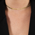 Colar dourado choker de fita em destaque, posicionado no pescoço. Tenure Semijoias