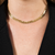 Colar dourado choker de seta exibido em um pescoço com pele clara. Tenure Semijoias