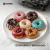 Plato con seis mini donas decoradas con diferentes coberturas y toppings, junto a una máquina para hacer mini donuts SUONO, ideal para desayunos y meriendas.