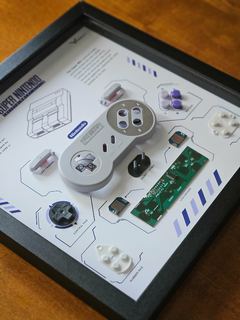 Quadro controle do videogame Super Nintendo (SNES) com as peças desmontadas e emoldurado
