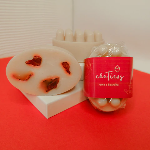 Sabonete massageador hidratante com fragrância frutada doce de romã e baunilha, com folhas naturais, embalado em celofane biodegradável, com rótulo vermelho escrito Cânticos.