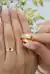 Par de alianças douradas com friso de 6mm, sendo uma das alianças segurada entre os dedos, com unhas decoradas ao fundo.