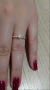 Par de alianças douradas com um friso e uma pedra de 6mm em um dedo, com unhas pintadas de vermelho ao fundo.