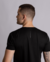 Homem usando camiseta preta, vista lateral, com detalhe de estampas nas costas da marca ÉKS WORKOUT.