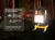 Reflector portátil Gadnic encendido en un bosque nocturno con tienda de campaña al fondo, mostrando sus características como ángulo ajustable, protección IP65 y cuatro funciones de luz