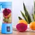 Mini liquidificador portátil azul com frutas dentro, ao lado de laranjas e uma fruta dragão cortada.