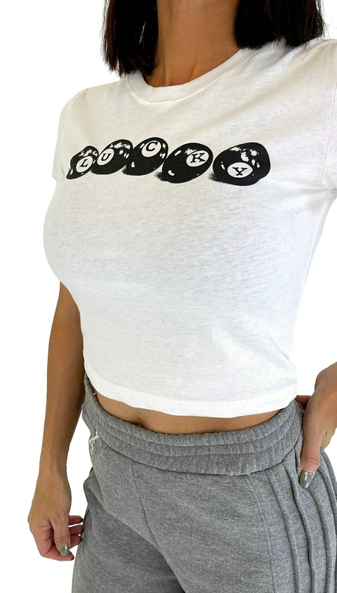Remera corta blanca de mujer con estampado "LUCKY" en bolas de billar, modelo vistiendo pantalón gris. Prenda de la categoría remeras y musculosas.