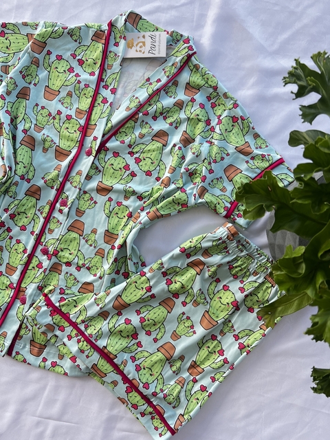 Conjunto de pijama estampado com cactos em vasos, em tons de verde e rosa, com detalhes em azul claro.