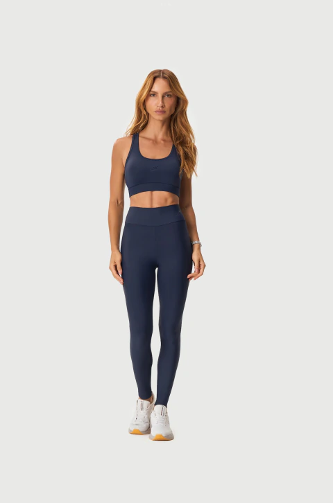 Mulher vestindo calça legging Power Mormaii azul marinho com top esportivo combinando e tênis branco