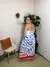 Mulher sorrindo usando um vestido longo branco com estampa de peixes azuis e detalhes em vermelho, posando em um ambiente interno.