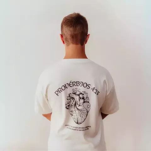 Camiseta cristã oversized branca com estampa de Provérbios 4:23 nas costas, mostrando um coração e uma ilustração relacionada.