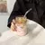 Vaso de vidrio ondulado de 500 cc con bebida fría y sorbete de vidrio, sostenido por una mano femenina sobre una mesa blanca