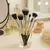 Set de brochas de maquillaje de 8 piezas en un vaso de vidrio, con fondo de productos de belleza.