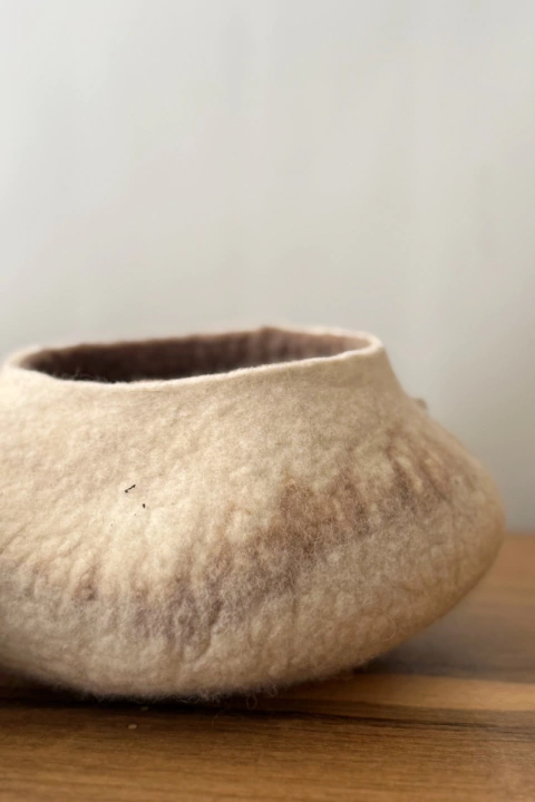 Cuenco NOMOS de fieltro en tonos beige y marrón sobre una mesa de madera