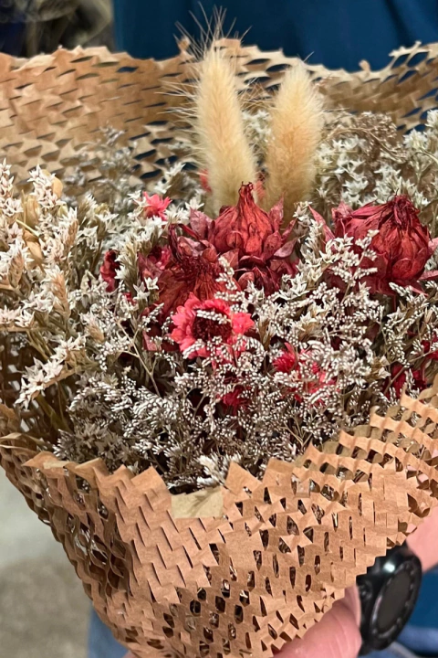 Ramo de flores secas con flores rojas y blancas, envuelto en papel de embalaje marrón texturizado