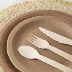 Juego de cubiertos de madera sobre platos de cartón, incluyendo un cuchillo, un tenedor y una cuchara.