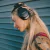Mulher usando fones de ouvido Bluetooth sem fio Polyvox XH-1029 na cor preta, com cabelo longo e tatuagens visíveis.