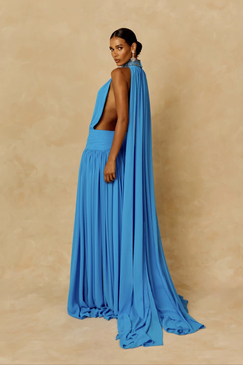 Mulher usando Vestido Áurea Bordado Longo azul, com gola alta bordada, capa integrada e saia fluida com fenda, do 2ARES Atelier.