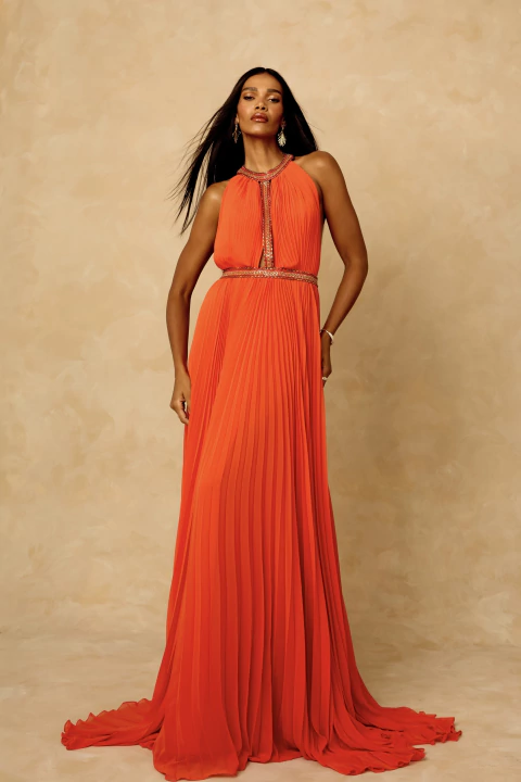 Modelo vestindo o Vestido Hera Bordado Longo em tom vibrante de tangerina, com plissado integral e gola halter bordada em pedrarias, caimento leve e elegante.