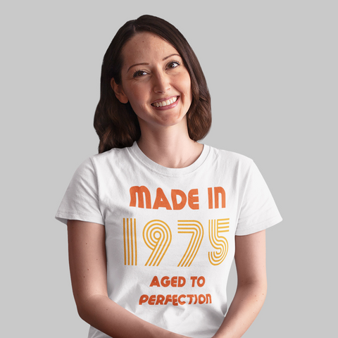 Mulher sorridente usando camiseta branca “Made in 1975 Aged to Perfection” em laranja.