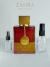 Frasco de perfume árabe feminino e unissex Armaf Club de Nuit Untold, com embalagem elegante de vidro vermelho, tampa dourada decorada com pedras e pingente dourado com a marca Armaf, acompanhado por dois frascos decants de spray transparente ao lado.