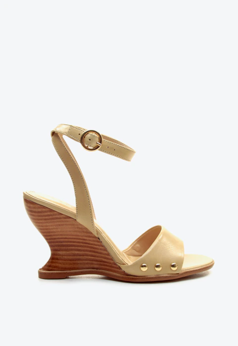 Sandália anabela em couro nude com salto arquitetônico e tachas douradas. Conforto e estilo para looks elegantes. Garanta já a sua peça exclusiva!
