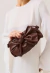 Bolsa tiracolo em couro marrom moka com laço volumoso, estilo pouch drapeado, alça com nós e fechamento por ímã. Sofisticação para qualquer ocasião!